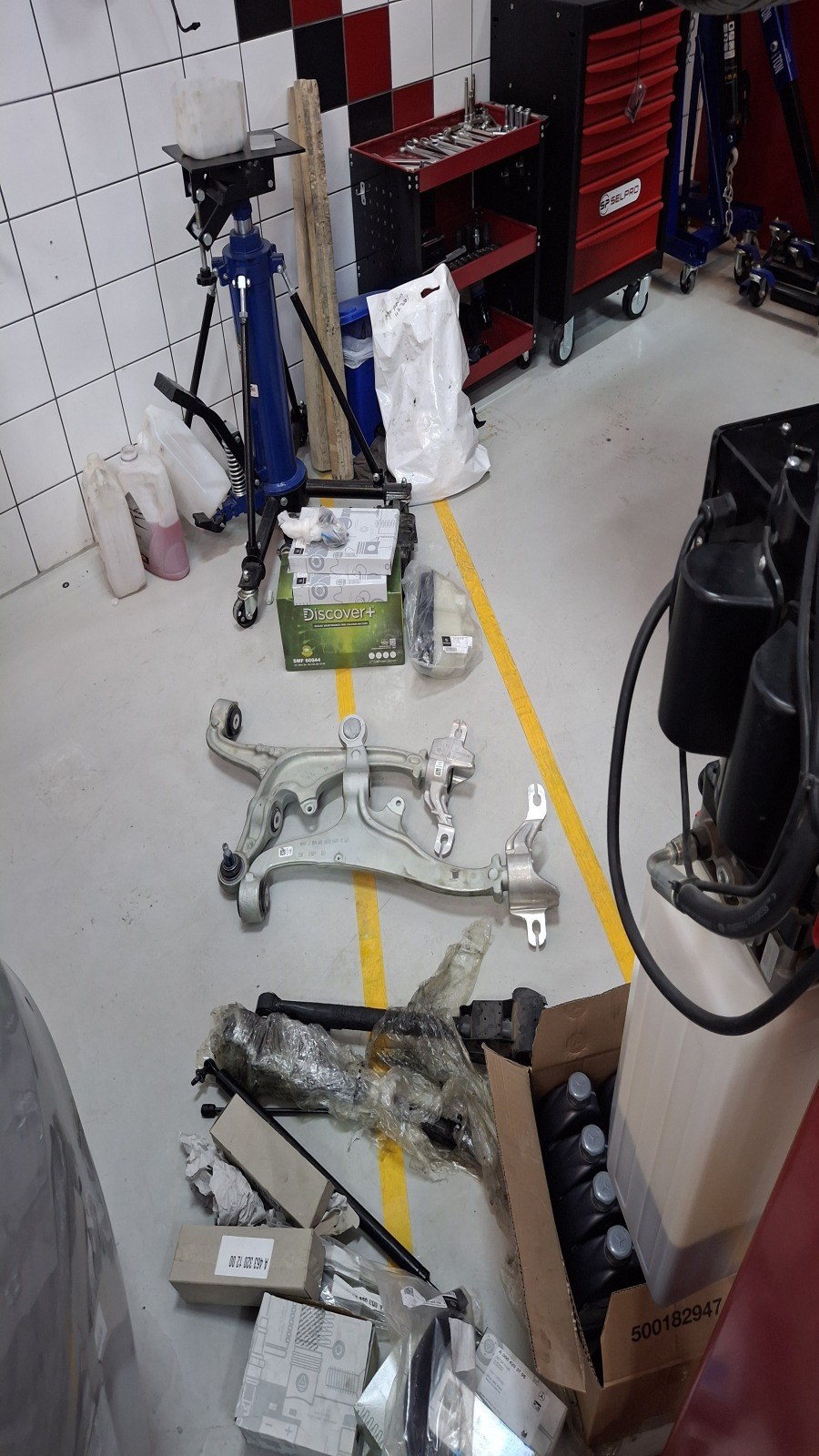Removed suspension control arms laid out next to the new parts boxes on the Velokar workshop floor