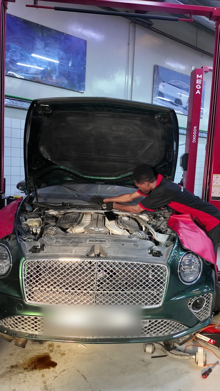Velokar technician working in the open engine bay of a green Bentley Continental GT in Al Quoz, Dubai