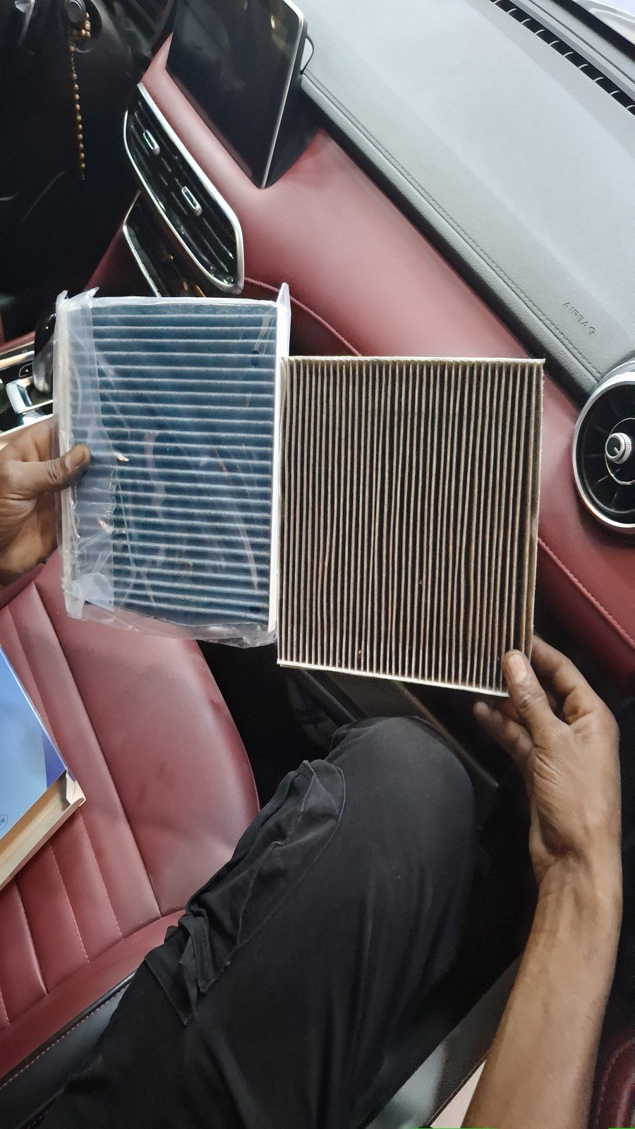 Old and new cabin air filters held side by side inside a Bentley with red leather interior at Velokar