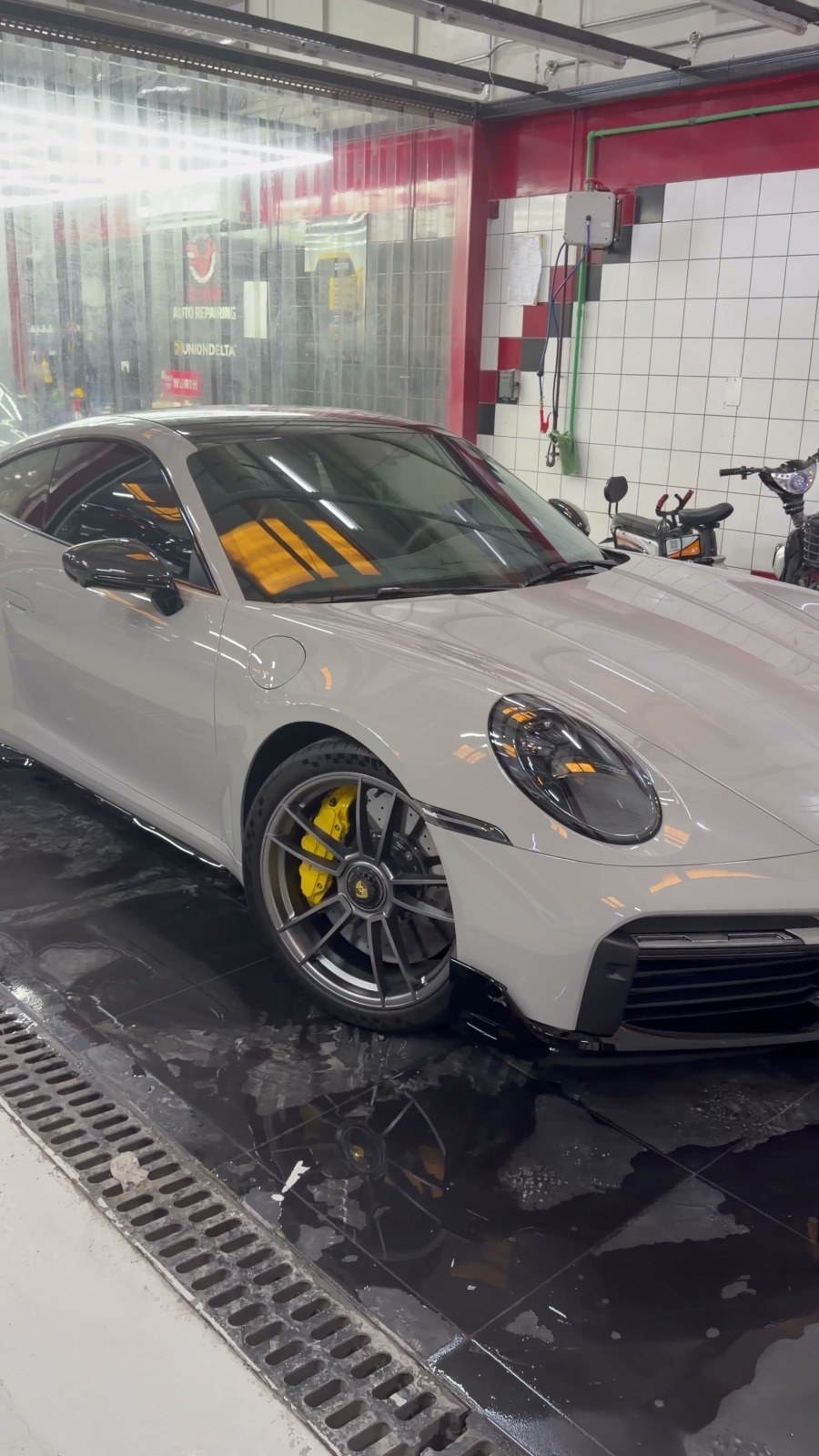 بورشه 911 بيضاء في ورشة فيلوكار بالقوز والكاليبر الأصفر ظاهر من خلال العجلة الأمامية
