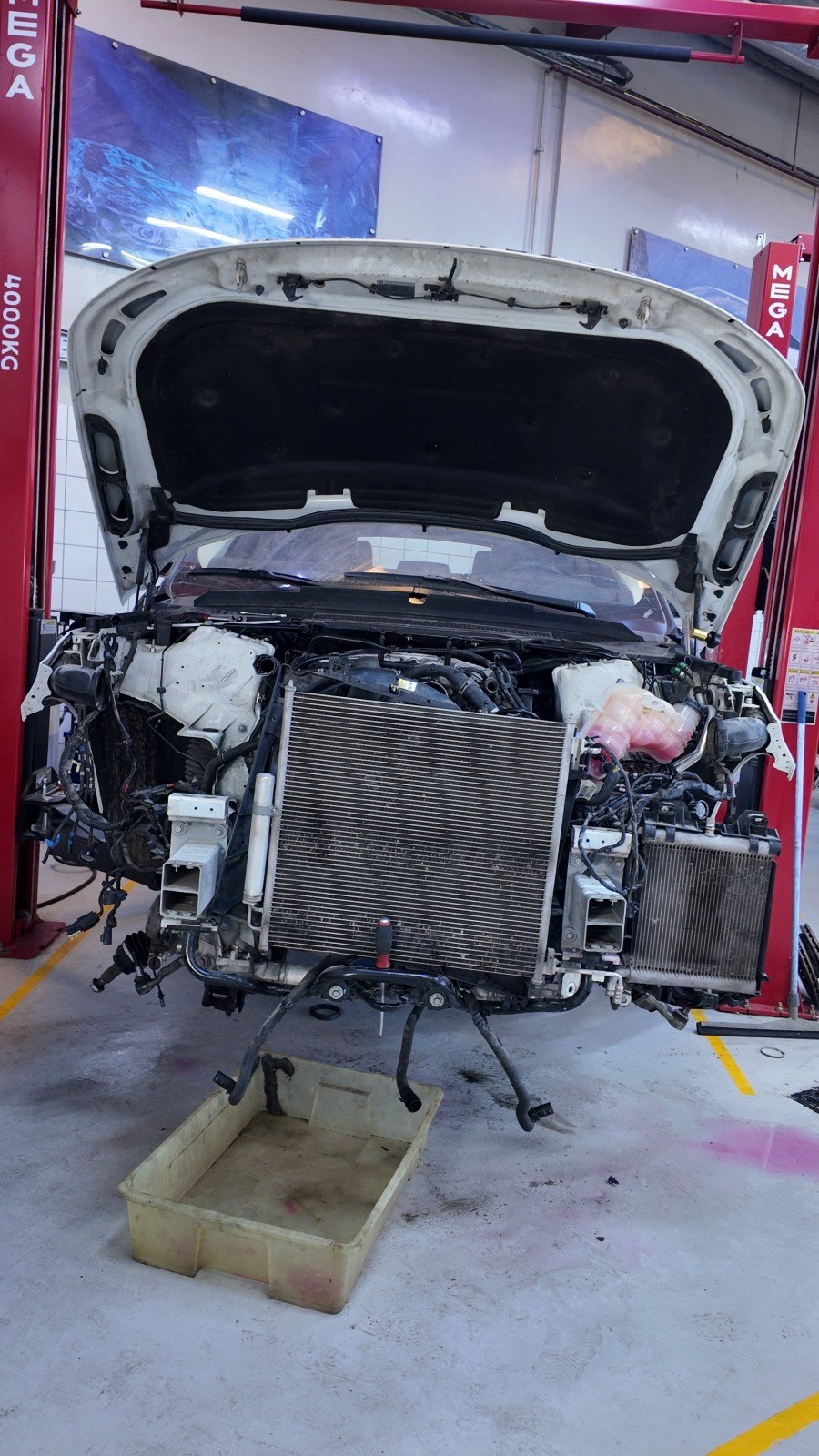 Front end of a white Range Rover stripped at Velokar with the condenser and radiator pack exposed on the lift