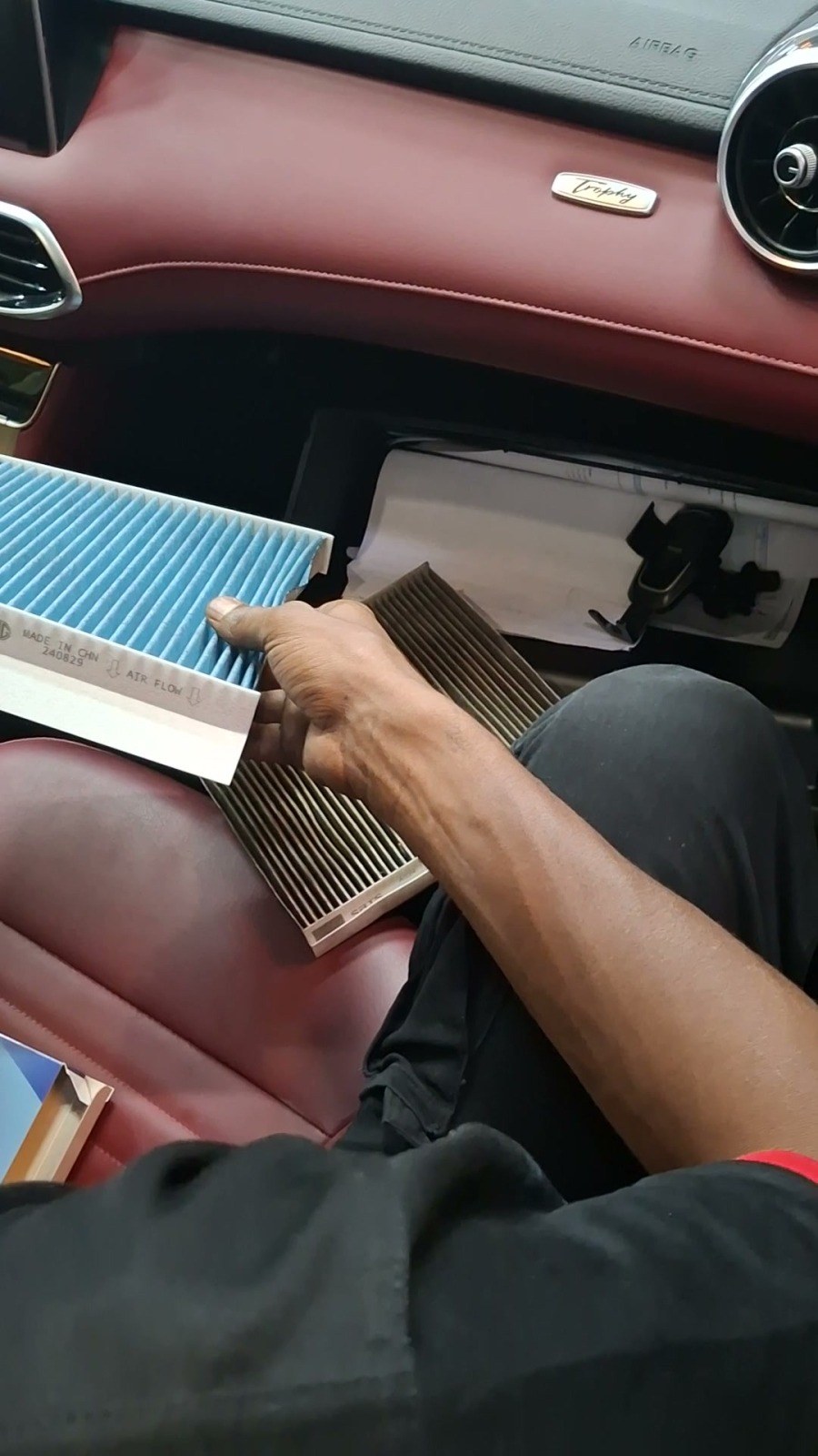 A clogged cabin air filter held next to a new one inside a Bentley with red leather, before replacement at Velokar