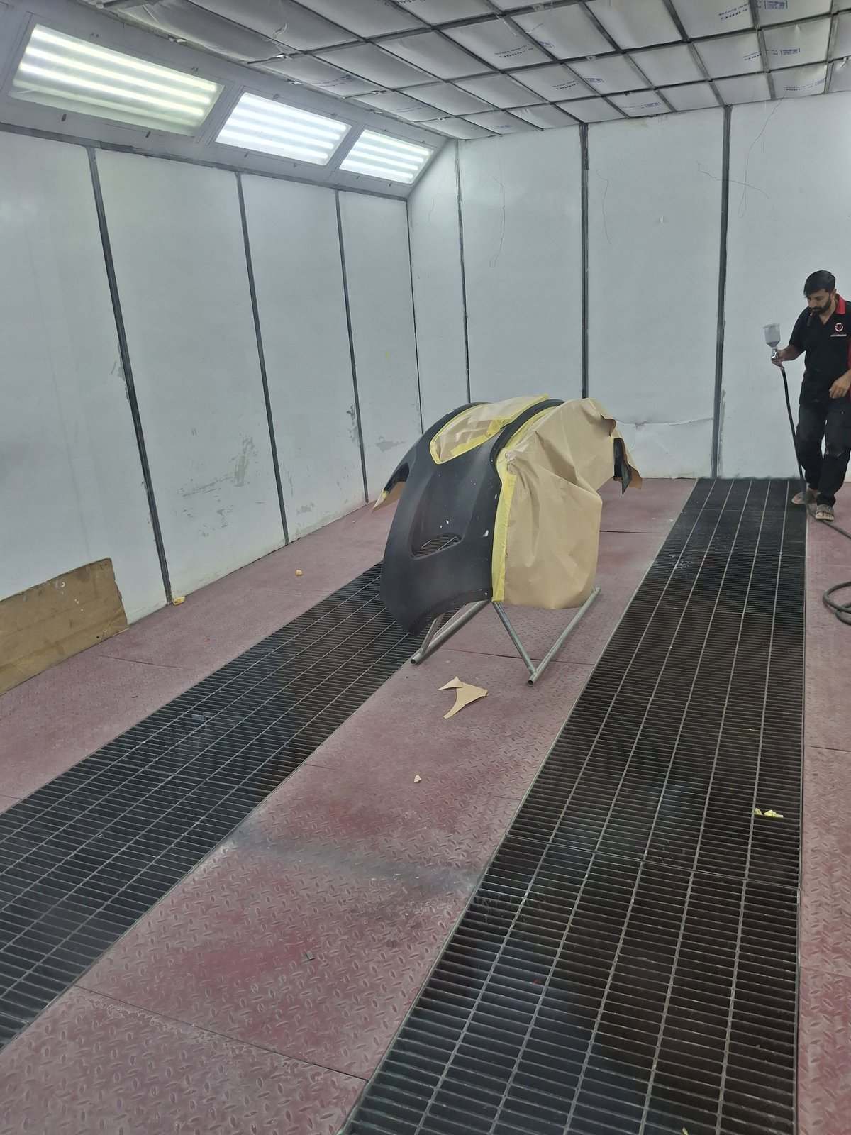 Technician spray painting a masked panel inside the Velokar paint booth