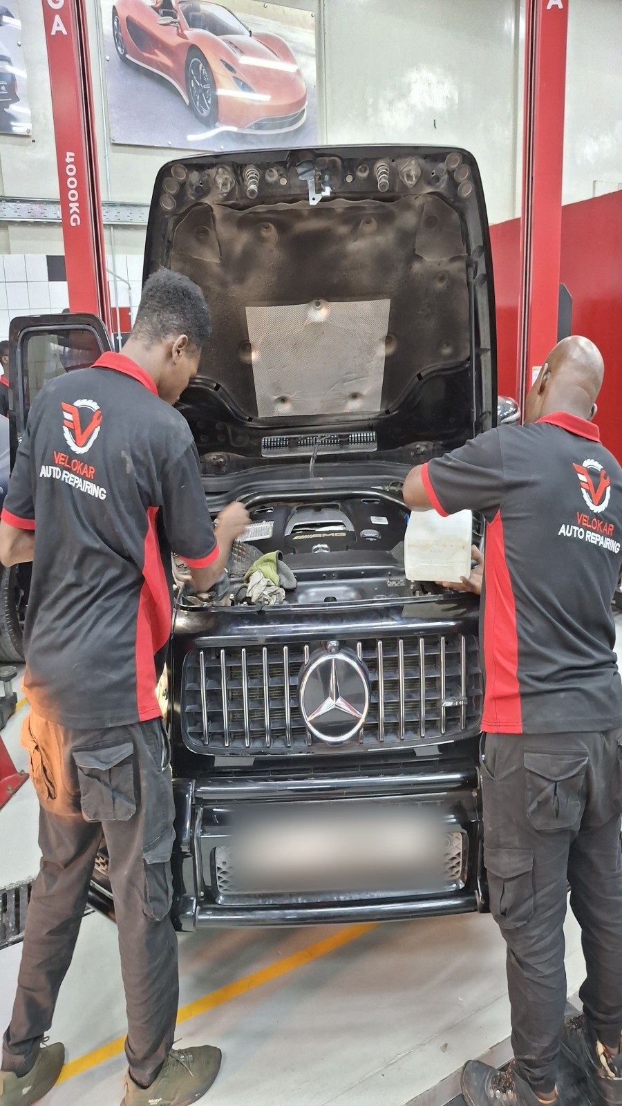 فنّيان من فيلوكار يفحصان حجرة محرّك مرسيدس G-Class سوداء بغطاء مرفوع