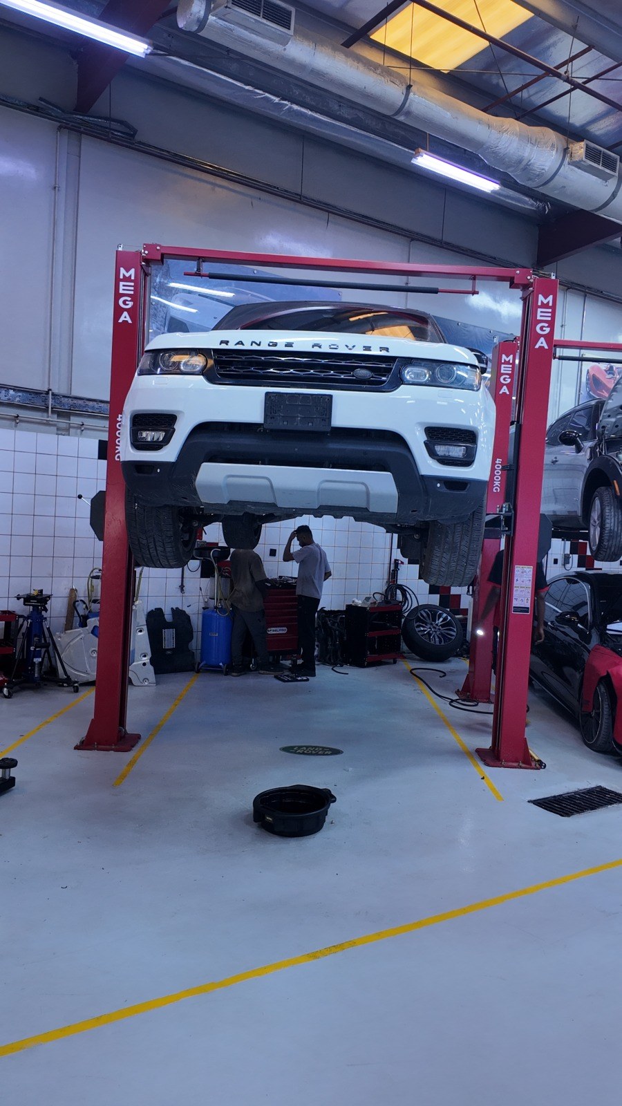 White Range Rover Sport raised on the two-post lift in the Velokar workshop, Al Quoz Industrial 3, with a drain pan on the floor