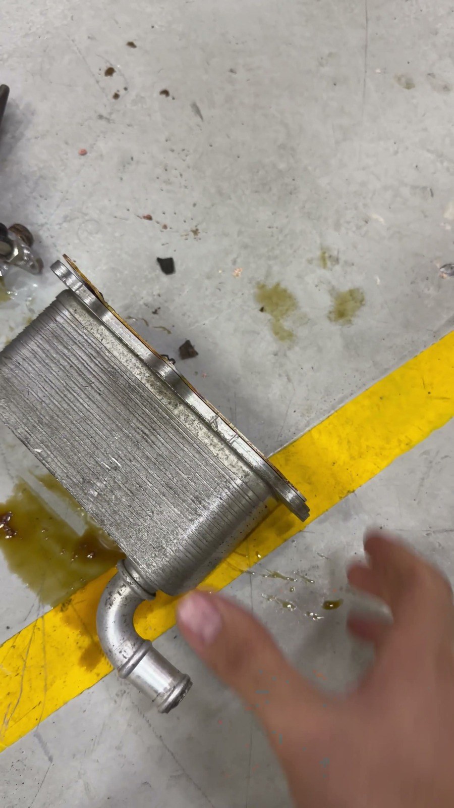 A removed engine oil cooler held up on the workshop floor at Velokar, oil still on its fittings
