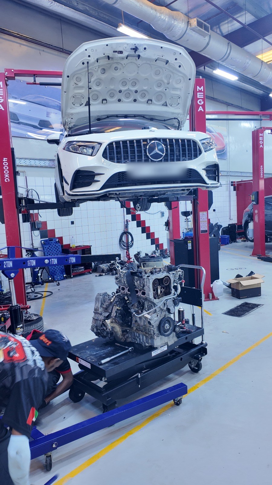 White Mercedes-AMG on the two-post lift at Velokar with its engine out on a stand beside it