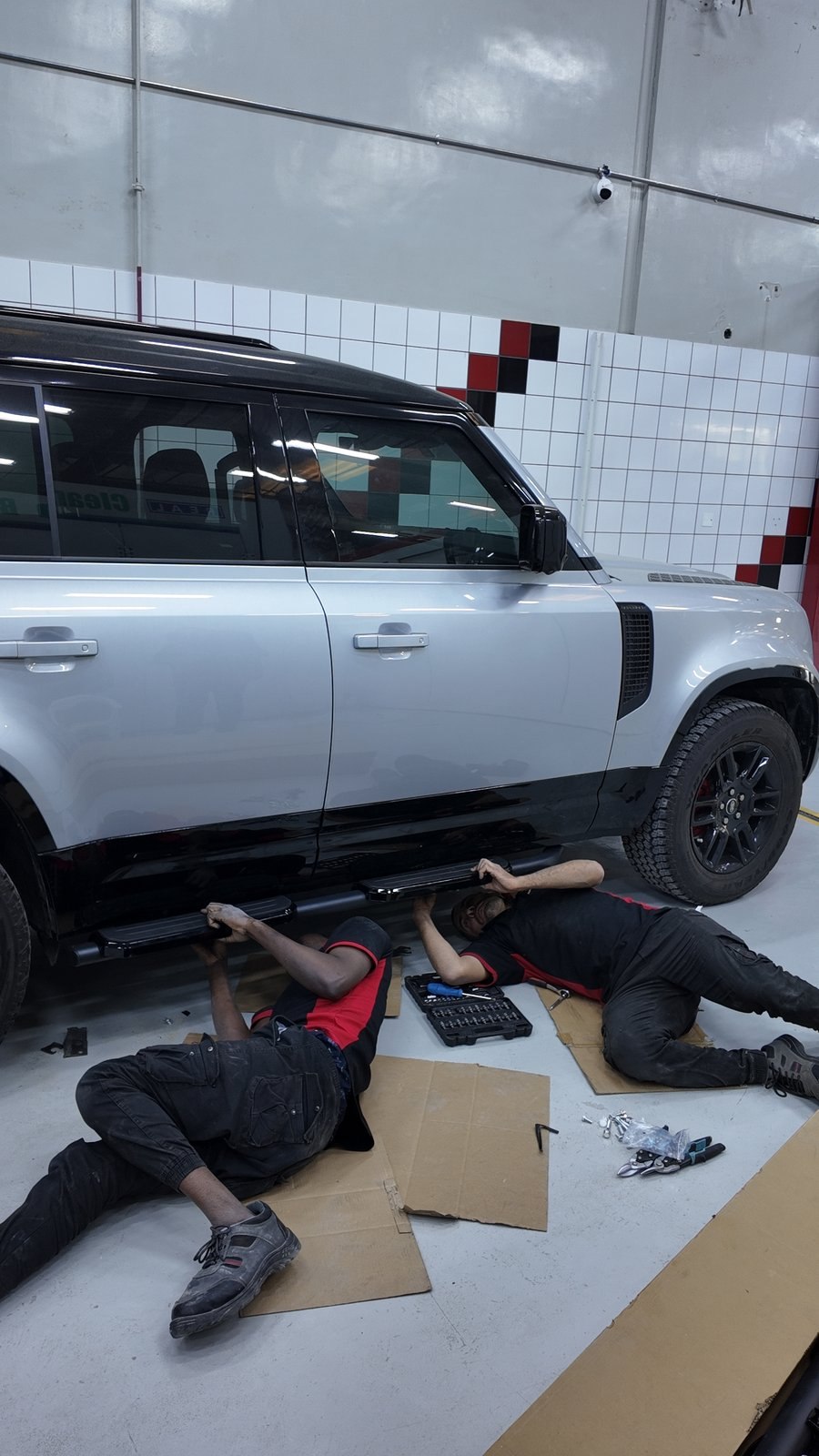 Two Velokar technicians working under a Land Rover Defender in Al Quoz